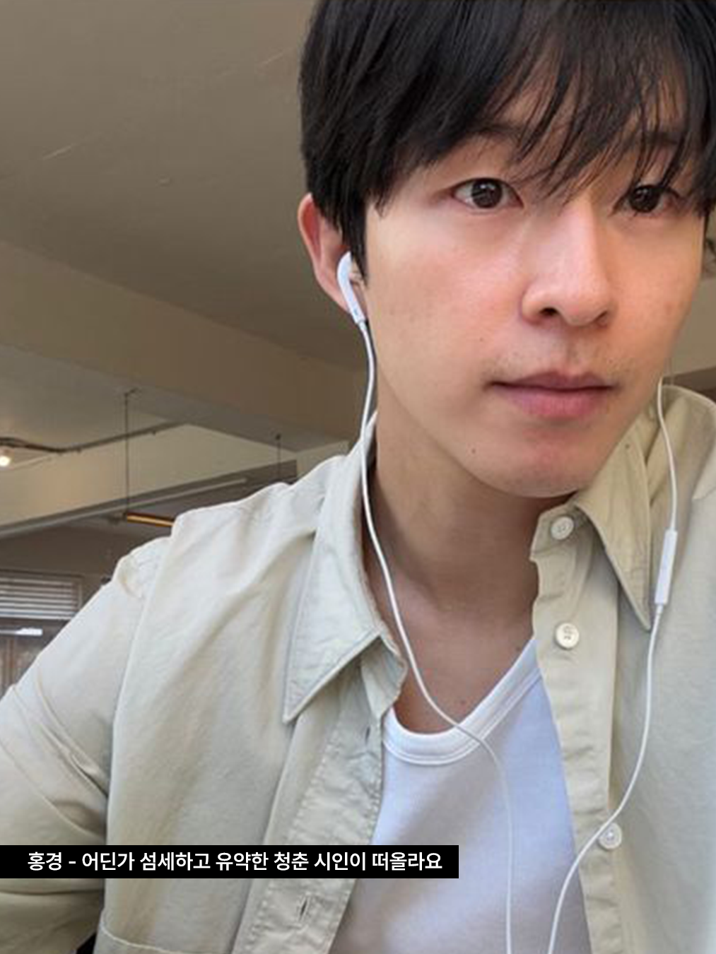 베이직 화이트 티셔츠 위에 연한 베이지색 셔츠를 레이어드하고, 줄 이어폰을 낀 배우 홍경의 사진