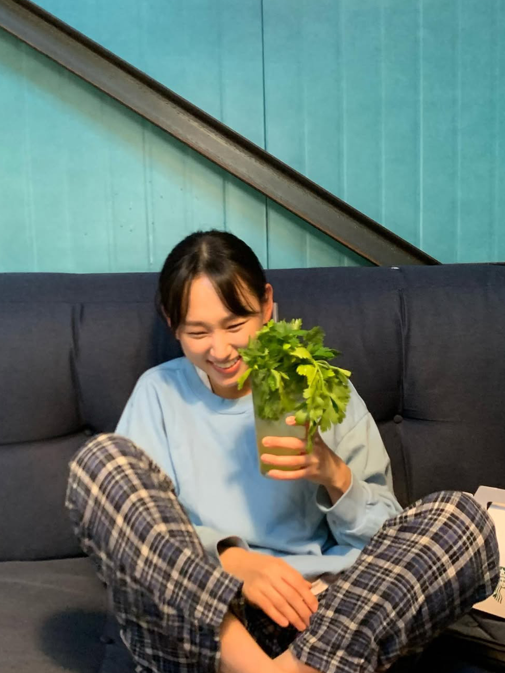 체크 무늬 파자마 팬츠와 소라색 니트 스웨터를 입고 식물을 들고 소파에 앉은 배우 류혜영의 사진