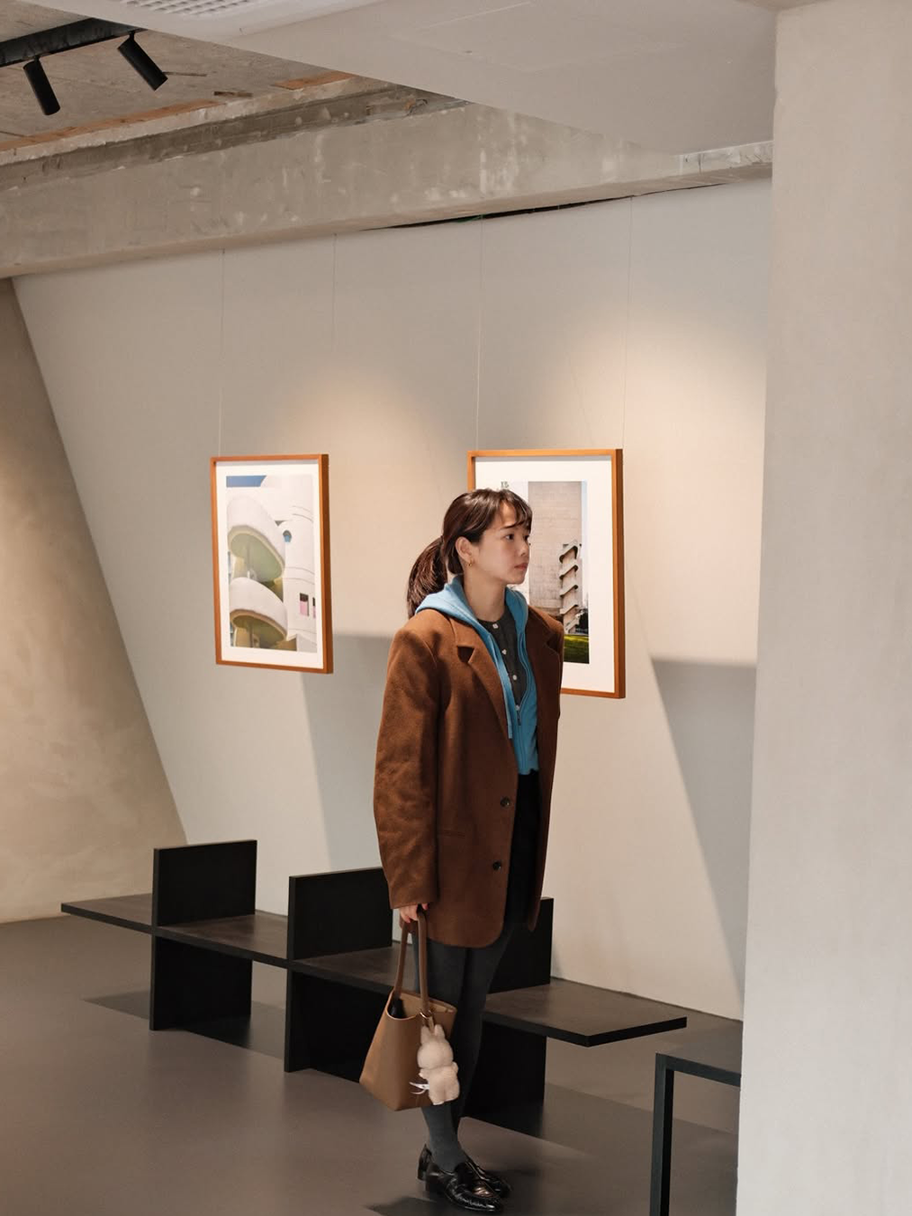 차콜 스타킹에 검은 로퍼, 블루 컬러의 후디와 브라운 색상의 울코트를 레이어링한 윤승아가 전시회를 관람하는 사진 